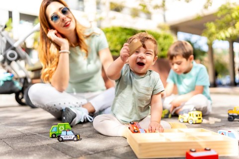 Baby holding a toy and laughing next to his family playing together on an urban park