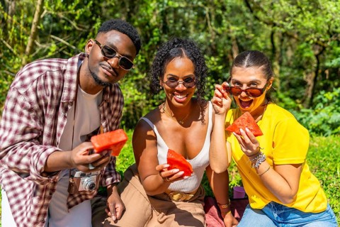 Three joyful friends enjoying fresh watermelon slices while relaxing at a sunny summer picnic in a