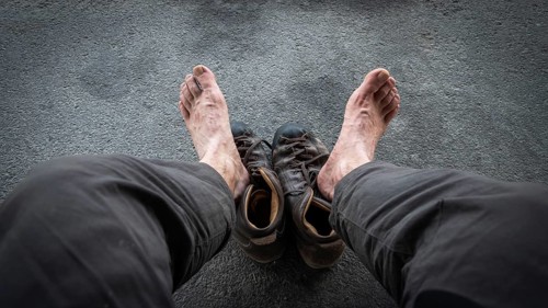 View of two bare feet of a pilgrim, worn hiking boots on dark ground, pilgrimage route Olavsweg or