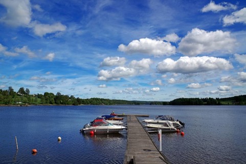 Lake with a wooden jetty and boats moored on it under a blue sky with white clouds, Stora Le,