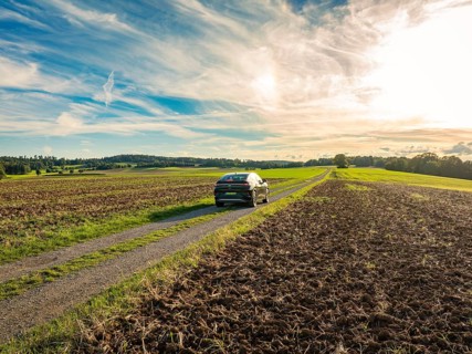 A car drives on a rural road between ploughed fields under a partly cloudy sky, Carsharing, VW ID5,