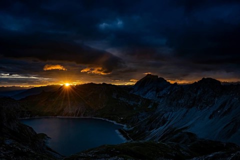 Lake Lüner See with Montafon mountains and dramatic cloudy sky at sunrise, Tschagguns, Rätikon,