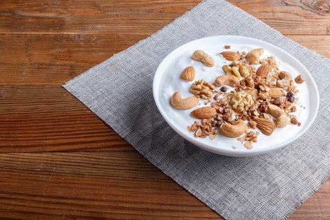 White plate with greek yogurt, granola, almond, cashew, walnuts on brown wooden background. close