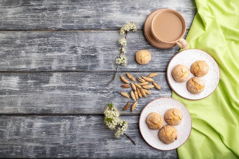 Almond cookies and a cup of coffee on a gray wooden background and green linen textile. Top view,
