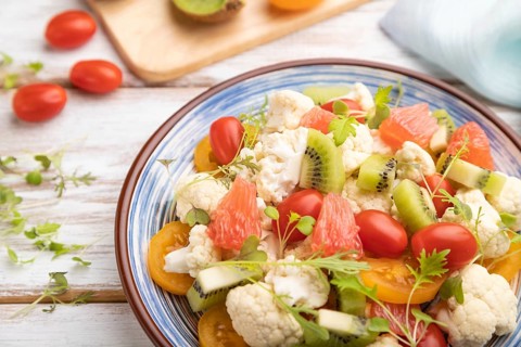 Vegetarian salad of cauliflower cabbage, kiwi, tomatoes, microgreen sprouts on white wooden