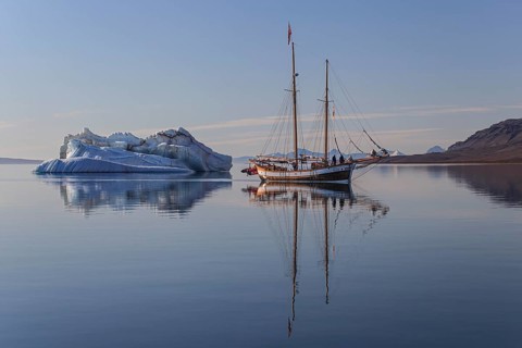 Traditional sailing ship reflected in fjord next to iceberg, sunny, Ittoqqortoormiit, Scoresby