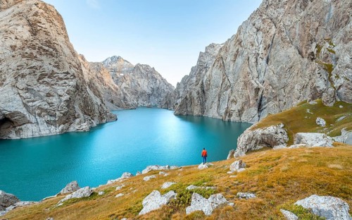 Young man at the turquoise mountain lake Kol Suu with rocky steep mountains, Kol Suu Lake, Sary