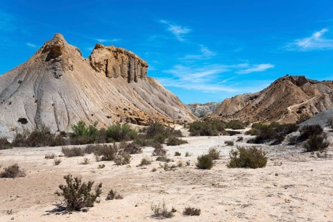 Dry desert landscape with sandy mountains and shrubs under a bright blue sky, Oasis de Lawrence de