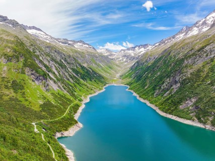 Blue lake, surrounded by high mountains and green, overgrown terrain under a bright blue sky, Klein
