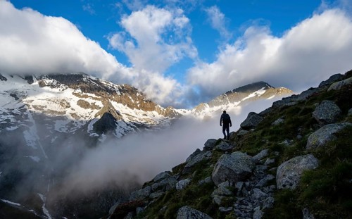 Silhouette of a mountaineer in front of a cloudy, atmospheric mountain landscape, rocky