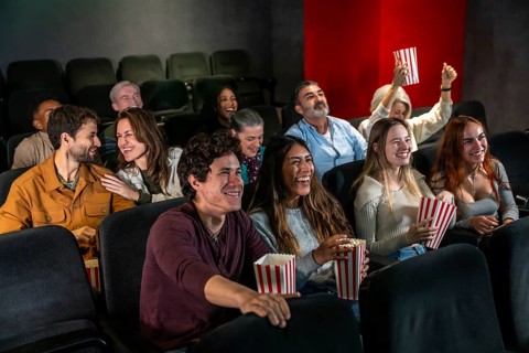 People of different ages and ethnicities are laughing and having fun while watching a movie at the