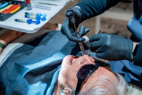 Dentist wearing black gloves injecting anesthesia to senior woman patient before dental procedure