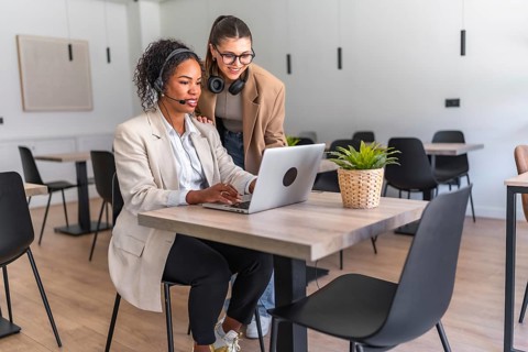 Two businesswomen collaborating on a laptop in a modern office, demonstrating teamwork and