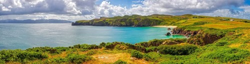 Panoramic view of a picturesque coastal landscape with cliffs, green grass and calm sea under a
