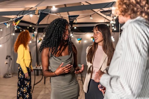 Multi-ethnic young people in elegant clothes chatting during night party at terrace