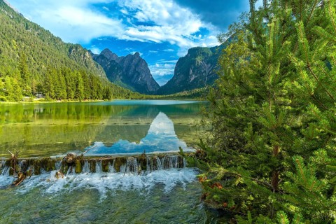 Crystal clear water cascading from a small waterfall into lake dobbiaco, reflecting the majestic