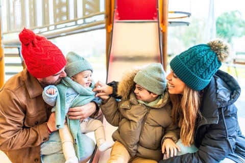 Cheerful family bundled in winter clothes enjoying quality time together while sliding down a