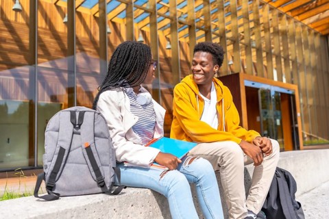 Two male and female african students talking sitting together in the university campus in a sunny