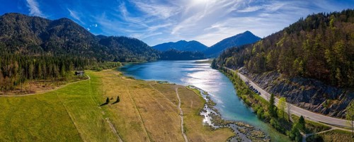 Picturesque panorama of a mountain lake with wooded hills and a road along the shore under a blue