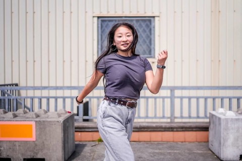 Asian woman dancing energetically k-pop style dance outside an industrial building