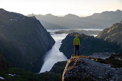 Mountaineer, young man standing on rocks and looking into the distance, at sunrise, fjord