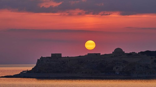 Sunrise, orange sunball over Venetian fortress, red sky, grey clouds, silhouette, backlight,