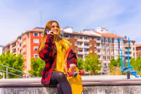 Skater woman in a yellow t-shirt, red plaid shirt and sunglasses, sitting with skateboard in the
