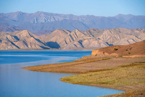 Blue Toktogul reservoir between dry mountain landscape, hilly mountains in the evening light,