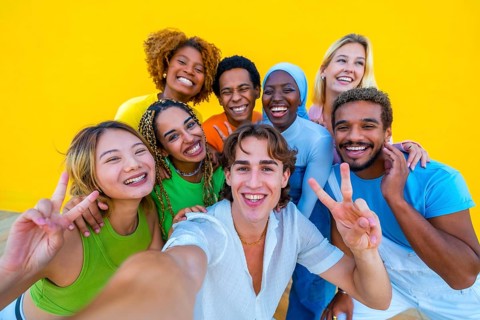 Multi-ethnic friends gesturing success while taking a selfie next to a yellow wall