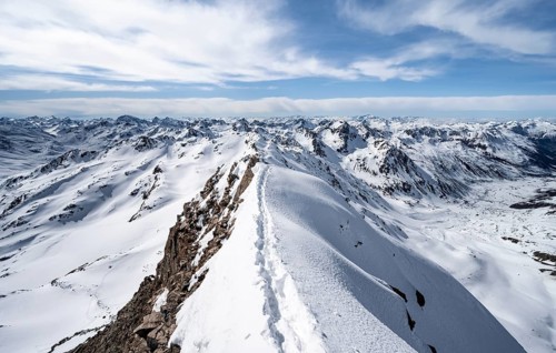 Tracks in the snow on a narrow mountain ridge in winter, summit of Piz Grialetsch, view of mountain
