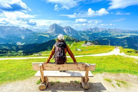 Hiker relaxing on a bench and admiring the odle mountains in val di funes, south tyrol, italy