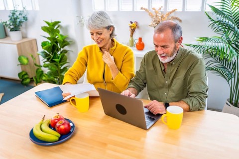 Happy senior couple working on personal financial bills at home using laptop sitting on the living