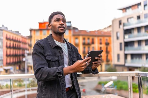 Casual young african man looking up while using digital tablet in the city
