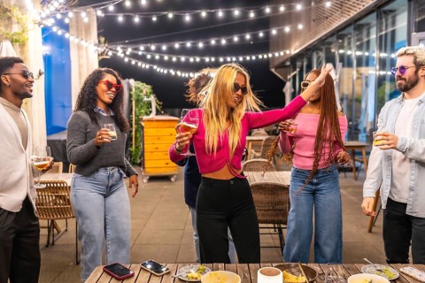 Blonde woman dancing among multi-ethnic friends at night party in a bar terrace in the city