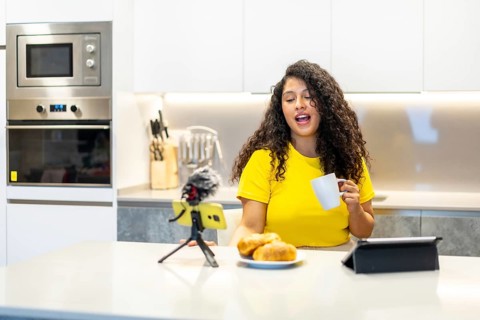 Female latin young and beauty content creator streaming online while having breakfast at home