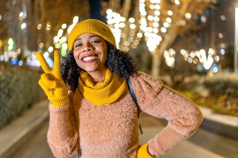 Portrait of a smiling young woman wearing yellow winter clothes showing victory sign with fingers