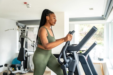 Businesswoman exercising on elliptical cross trainer in hotel gym, maintaining healthy lifestyle