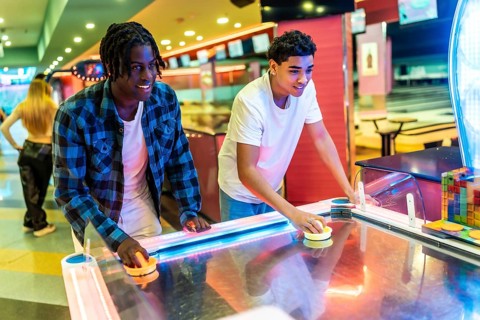 Two young men concentrating on playing air hockey in a vibrant entertainment center, enjoying a