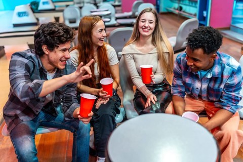 Four young multiethnic friends are laughing and having fun while sitting in a bowling alley,