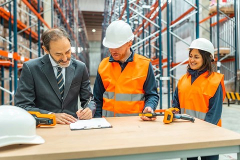 Manager signing delivery notes in a logistics warehouse, assisted by two warehouse workers using