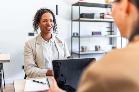 Two businesswomen smiling and discussing strategy during a meeting in the office using a laptop