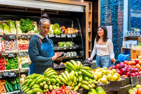 Grocery store employee using a digital tablet for inventory management of fresh fruits and