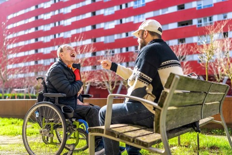 Two men enjoying time together in urban park, one using wheelchair, demonstrating inclusion and