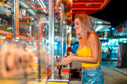 Excited blonde woman having fun playing arcade games at fair at night