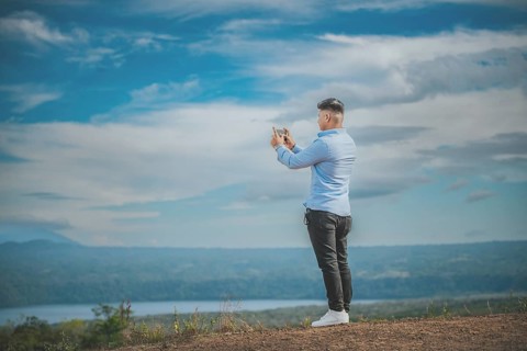 Young man taking photos with cell phone at a natural viewpoint. Tourist taking photos with phone at