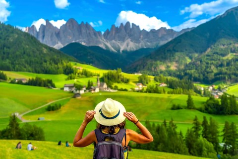 Female tourist holding her hat while looking at st. Magdalena church in val di funes with the odle