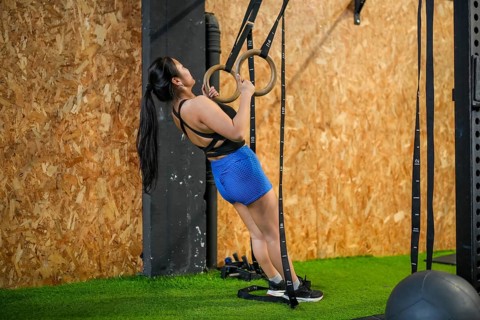 Full length side view of an asian woman exercising using gym rings to do pull-ups