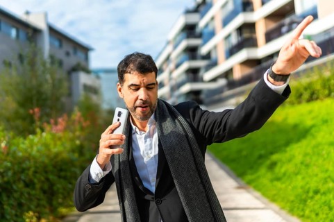 Businessman enjoying day in the city dancing and celebrating while holding a smartphone