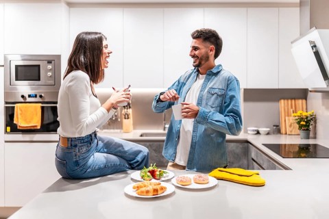 Young couple laughing and talking while having breakfast and coffee in their modern kitchen