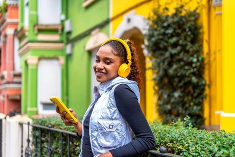 Happy african american woman using phone and listening to music in the city next to colorful houses